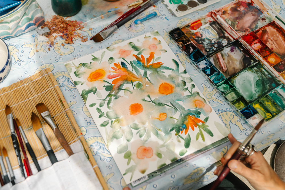 Overhead view of floral watercolor painting with palette and brushes, illustrating blending and layering from a watercolor techniques cheat sheet.