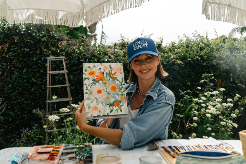 Artist holding a completed floral watercolor painting outdoors while teaching a back to school guide for artists.