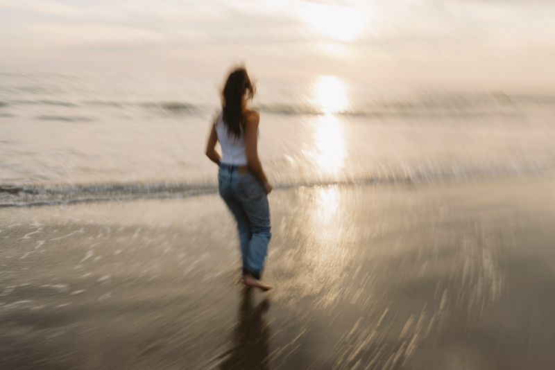 Artist standing on coastal rocks at sunset, observing natural light and inspiration for painting water reflections.