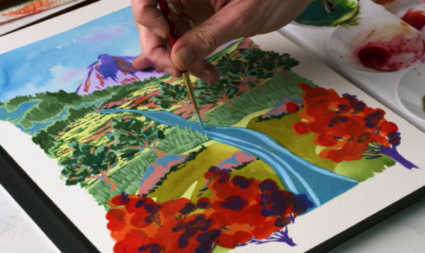 Artist painting a vibrant landscape scene with mountains, river, and flowers in a watercolor travel journal.