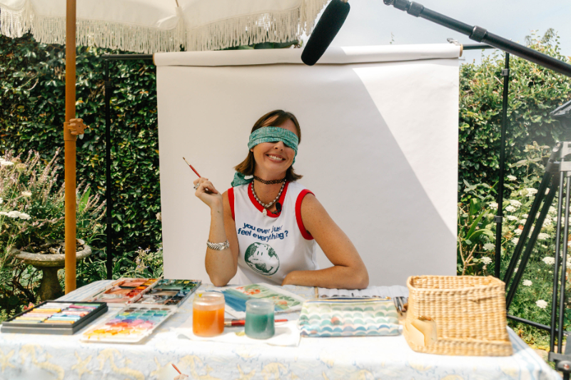 Artist smiling while painting with a blindfold on during a blindfold challenge to build creative confidence and trust intuition.