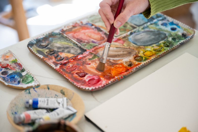 Close-up of a watercolor palette filled with vibrant paints as a brush mixes colors for a watercolor paint night.