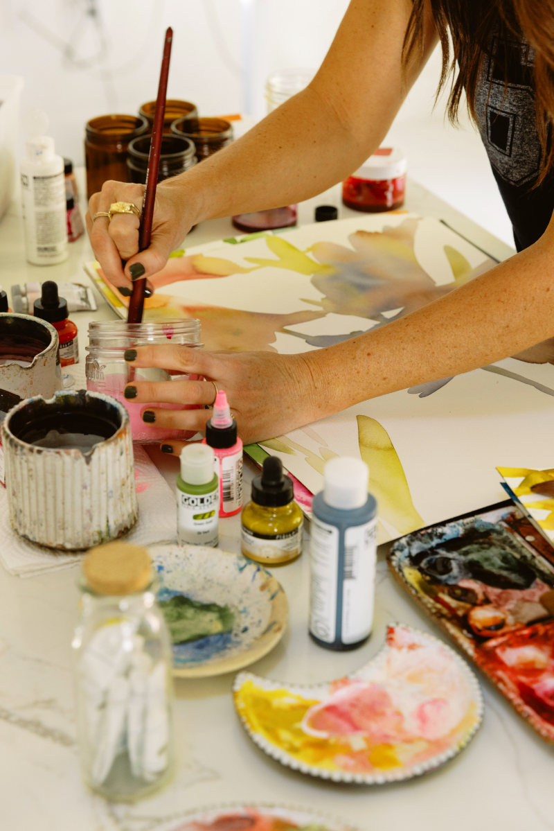 Artist dipping a brush into water while preparing supplies for a cozy watercolor paint night at home.