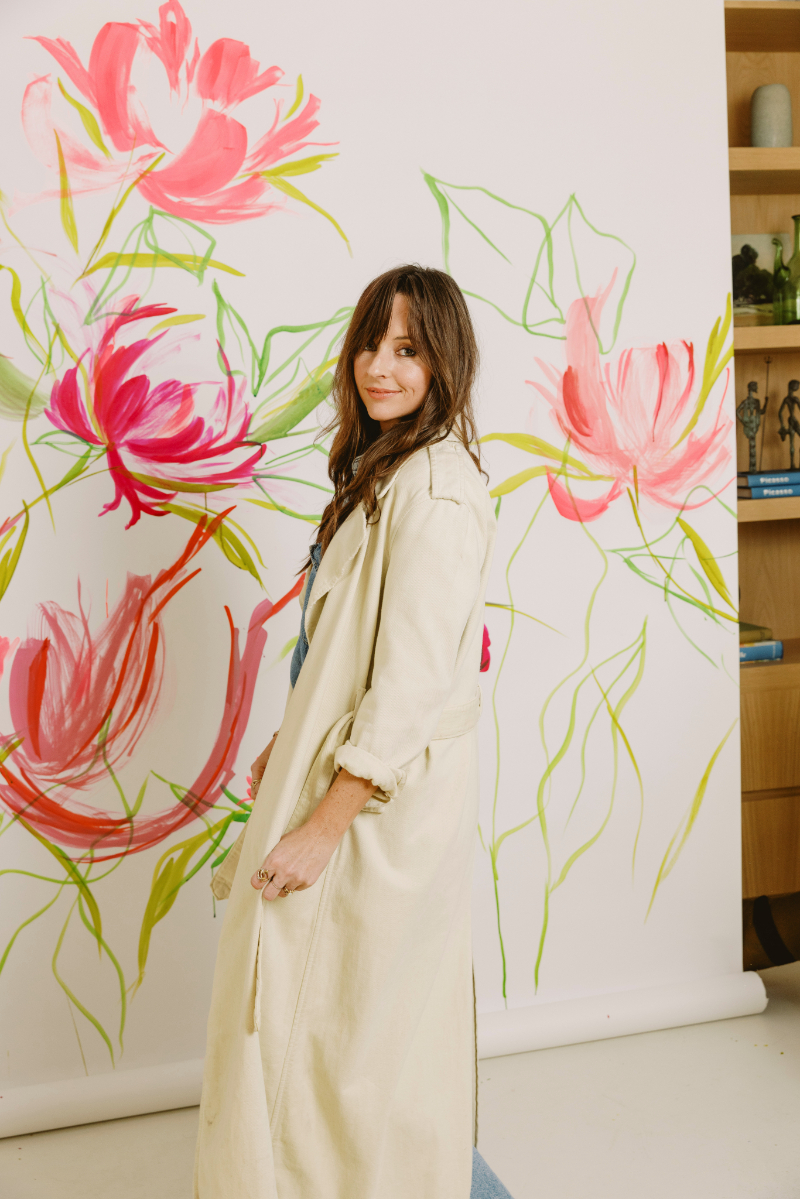 Artist standing in front of a large floral painting inspired by loose brushwork and expressive watercolor washes.
